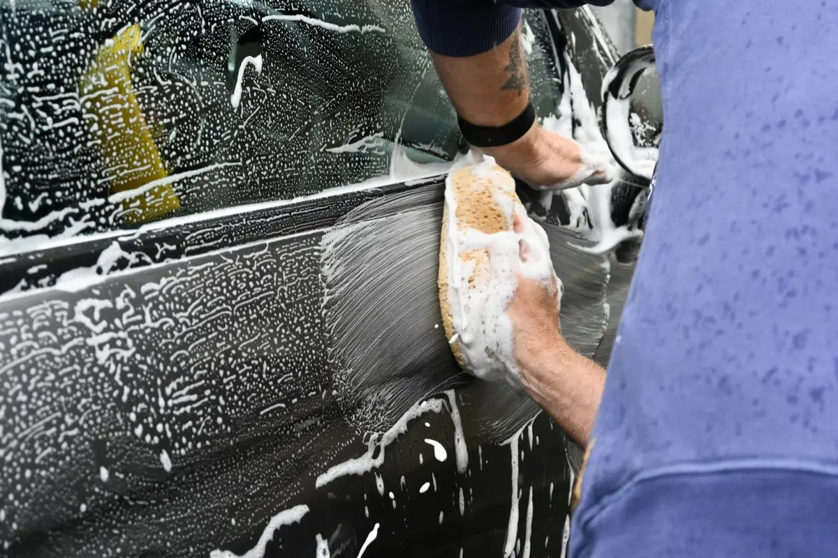Le patron lave une carrosserie à la main avec une éponge et de la mousse